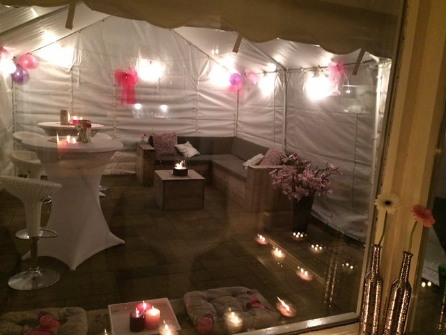 Partytent van 4 × 6 meter tegen een woning, met statafels, barkrukken, verlichting en verwarming.