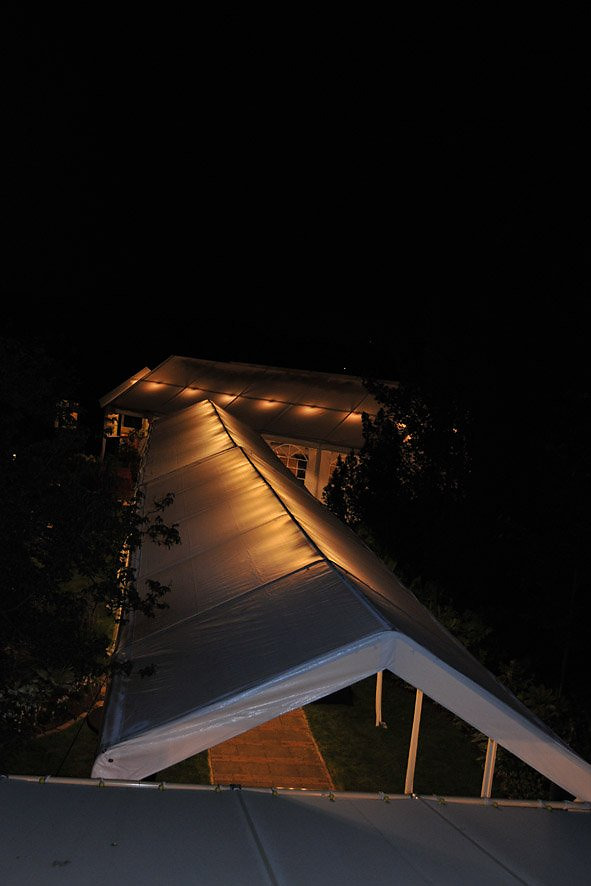 Overdekte route naar een trouwlocatie, met gekoppelde tenten en sfeerverlichting.