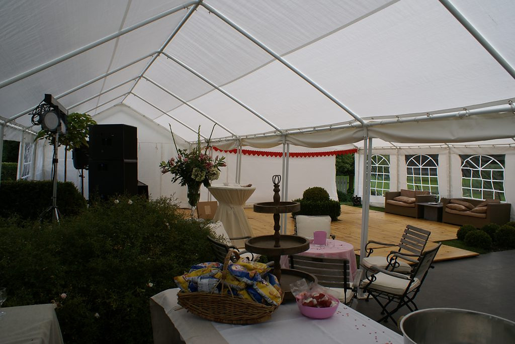 Twee gekoppelde tenten vormen een overkapping van 10 × 12 meter, met houten vloer en sfeerverlichting.