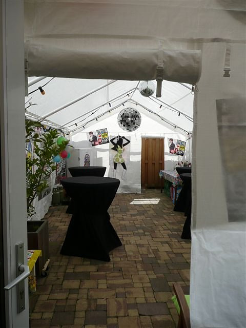 Partytent van 4 × 8 meter aansluitend op de woning, met statafels en rokken.