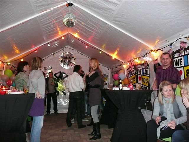 Partytent van 4 × 8 meter aansluitend op de woning, met statafels en rokken.